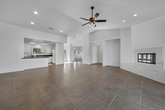 unfurnished living room featuring ceiling fan, a premium fireplace, dark tile patterned flooring, and vaulted ceiling