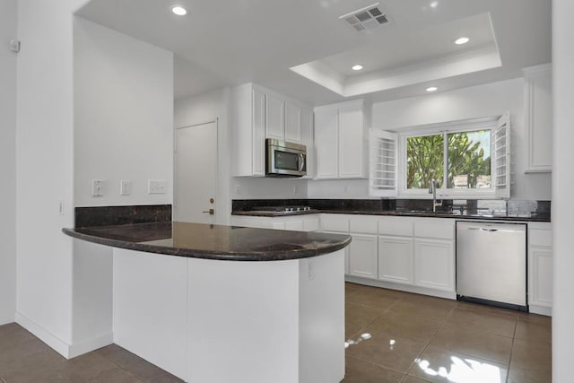 kitchen with sink, appliances with stainless steel finishes, white cabinetry, kitchen peninsula, and a raised ceiling