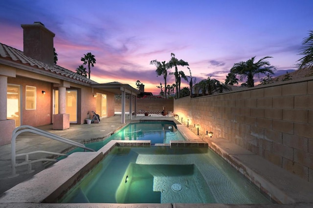 pool at dusk with an in ground hot tub and a patio