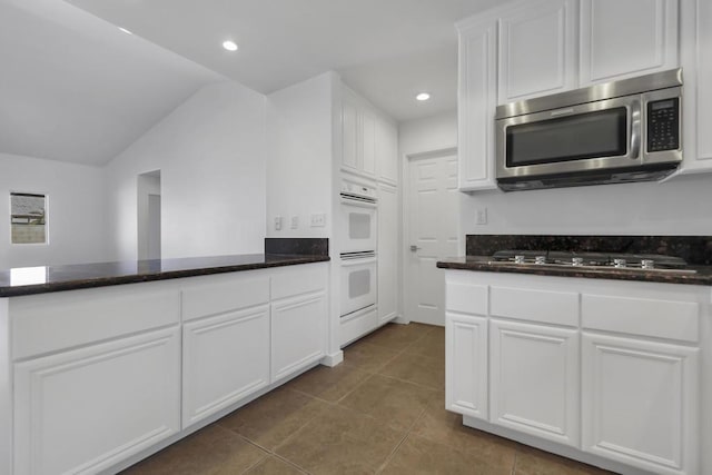 kitchen with tile patterned flooring, lofted ceiling, appliances with stainless steel finishes, and white cabinets