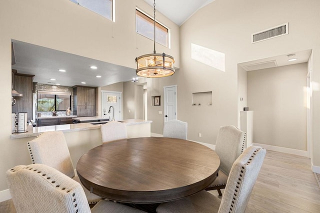 dining area with high vaulted ceiling, light hardwood / wood-style flooring, a chandelier, and sink