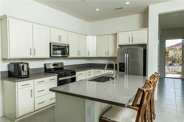 kitchen featuring sink, a breakfast bar area, appliances with stainless steel finishes, white cabinets, and a center island with sink