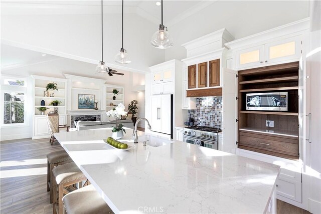 kitchen with built in appliances, white cabinets, hanging light fixtures, and a large island