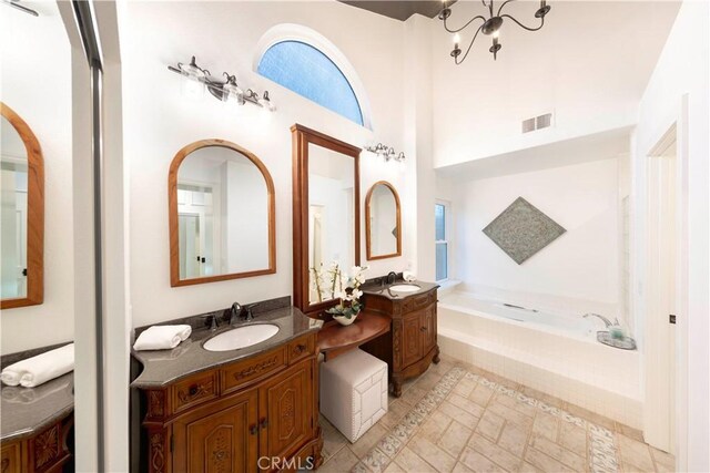 bathroom featuring a notable chandelier, tiled tub, and vanity