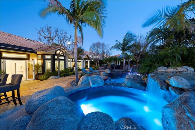 pool at dusk featuring a patio and a hot tub