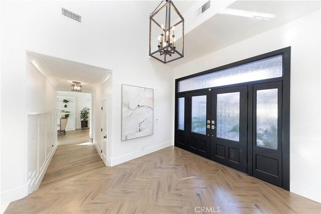 foyer entrance featuring french doors, an inviting chandelier, and light parquet floors