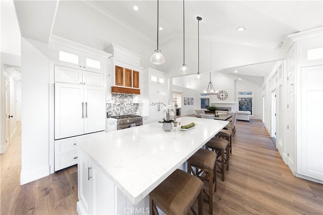 kitchen with decorative light fixtures, a center island with sink, lofted ceiling, and white cabinetry