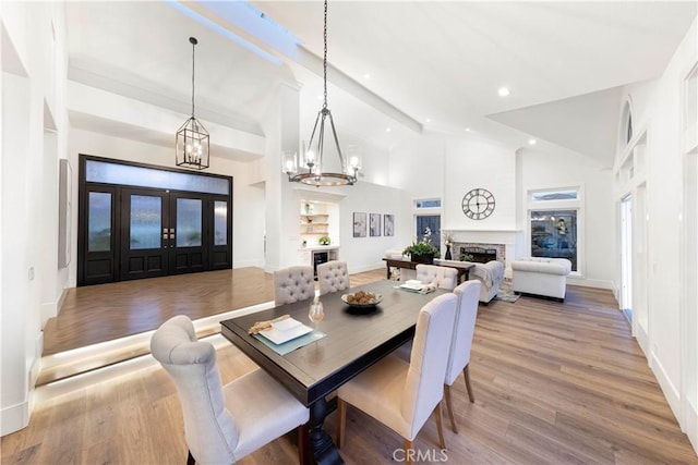 dining room featuring hardwood / wood-style floors, a towering ceiling, beamed ceiling, french doors, and built in features