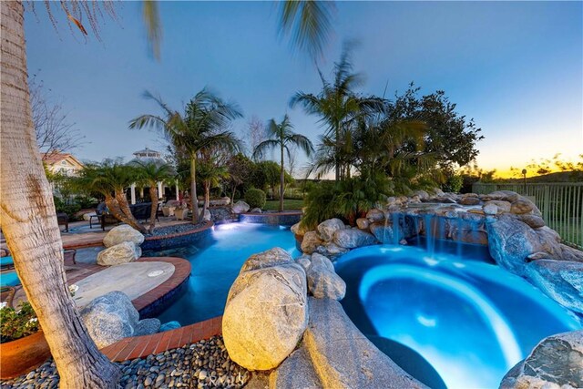 pool at dusk featuring an in ground hot tub