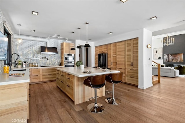 kitchen with sink, decorative light fixtures, black fridge, stainless steel double oven, and a kitchen island