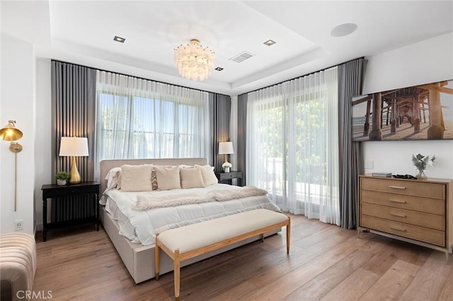 bedroom featuring light hardwood / wood-style floors, an inviting chandelier, radiator heating unit, and a tray ceiling