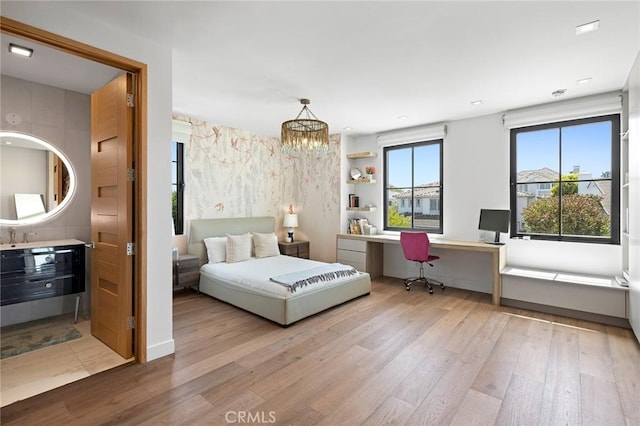 bedroom with a notable chandelier, built in desk, and light hardwood / wood-style floors