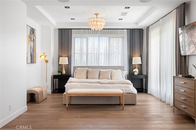 bedroom with a tray ceiling, light hardwood / wood-style flooring, and a chandelier