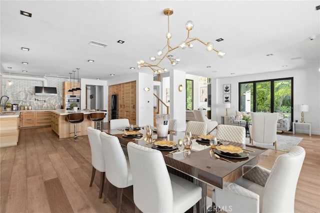 dining area with sink, light hardwood / wood-style floors, and a notable chandelier