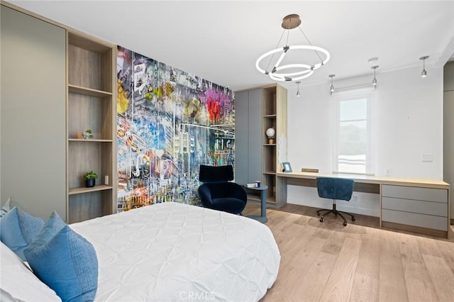 bedroom featuring built in desk, an inviting chandelier, and light hardwood / wood-style floors