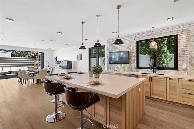 kitchen featuring a center island, light brown cabinetry, a kitchen bar, sink, and light hardwood / wood-style flooring