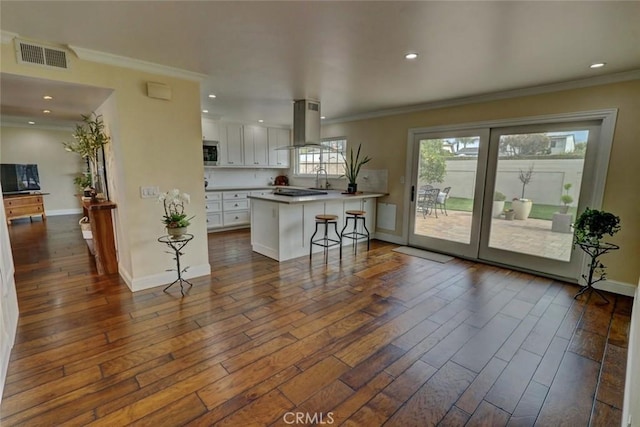 kitchen with dark hardwood / wood-style floors, island range hood, white cabinetry, a kitchen bar, and a center island