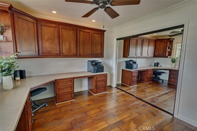 office featuring wood-type flooring, ornamental molding, built in desk, and ceiling fan