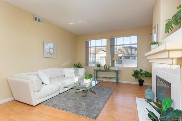 living room with a tiled fireplace and light wood-type flooring