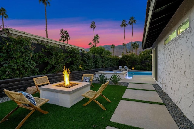 patio terrace at dusk with a fenced in pool, an outdoor fire pit, and a lawn