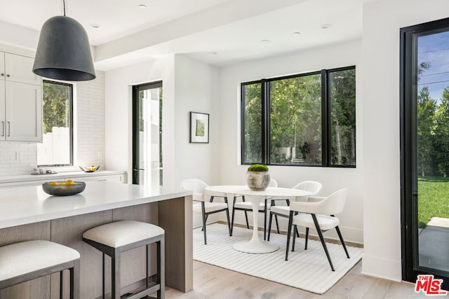 kitchen featuring decorative light fixtures, light wood-type flooring, backsplash, and white cabinetry