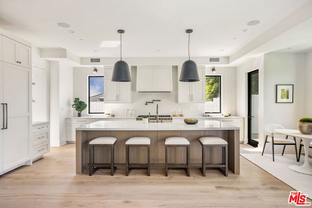 kitchen featuring white cabinets, light wood-type flooring, and an island with sink