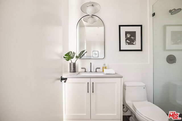 bathroom with toilet, a shower, vanity, and tile walls