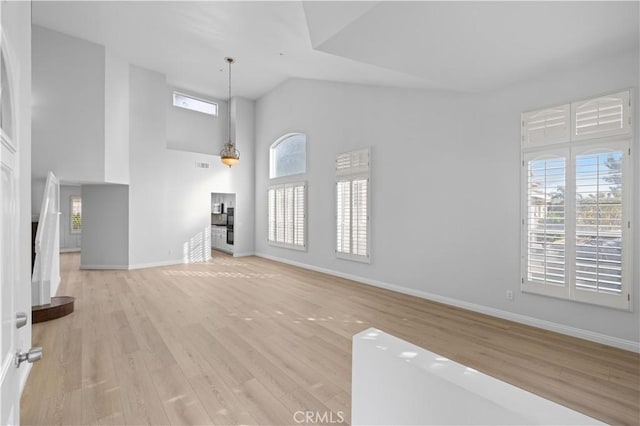 unfurnished living room with light hardwood / wood-style floors and a towering ceiling