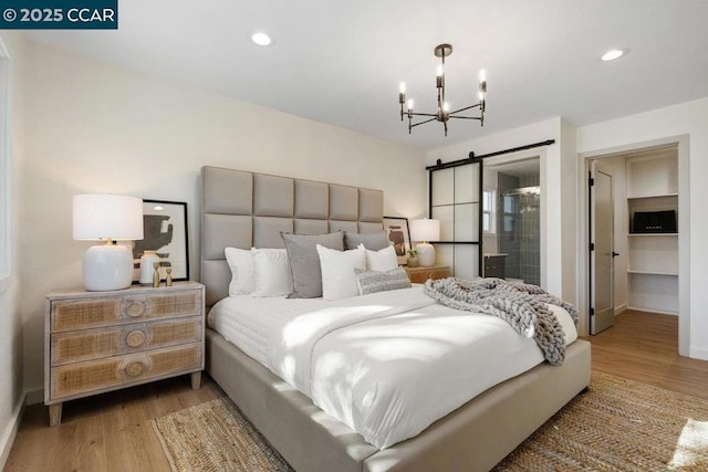 bedroom with light wood-type flooring, ensuite bathroom, an inviting chandelier, and a barn door