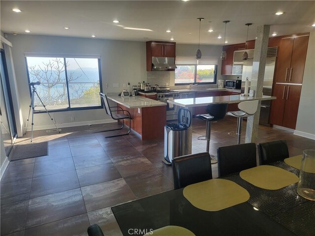 kitchen featuring a kitchen breakfast bar, stainless steel appliances, light countertops, and under cabinet range hood