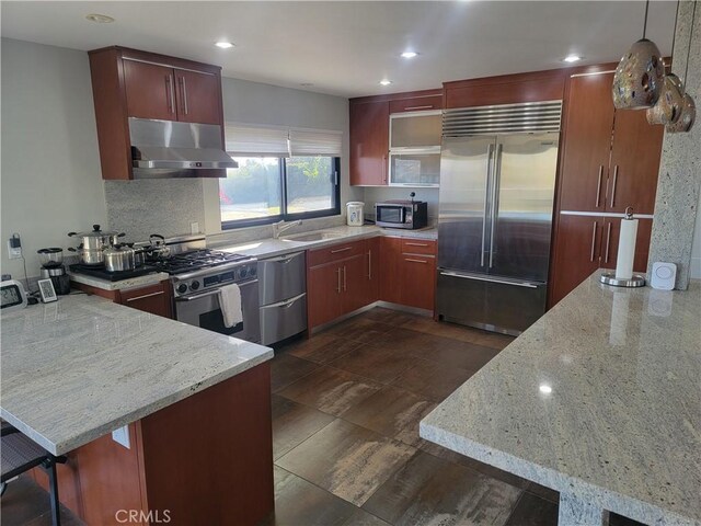 kitchen featuring under cabinet range hood, a peninsula, a sink, appliances with stainless steel finishes, and decorative backsplash