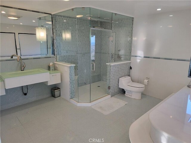 bathroom featuring tile walls, toilet, a sink, a shower stall, and tile patterned floors