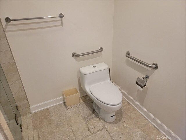 bathroom with toilet, a shower with door, and baseboards