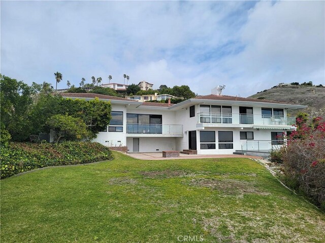 rear view of property featuring a yard, a patio area, a balcony, and stucco siding