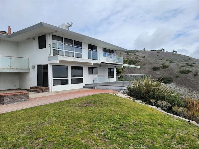 rear view of property featuring a yard, a patio area, a balcony, and stucco siding