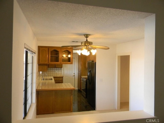 kitchen with kitchen peninsula, black fridge with ice dispenser, tile countertops, backsplash, and sink