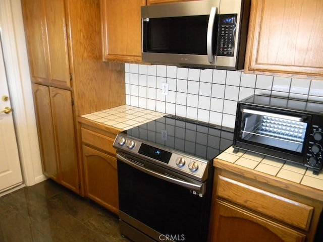 kitchen with stainless steel appliances, tile countertops, dark tile patterned flooring, and tasteful backsplash