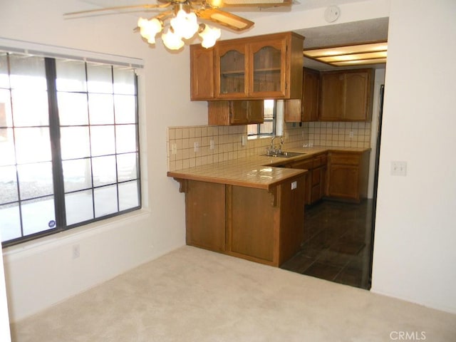 kitchen with kitchen peninsula, tile countertops, tasteful backsplash, ceiling fan, and sink