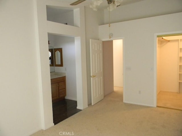 unfurnished bedroom with connected bathroom, ceiling fan, a closet, carpet floors, and a high ceiling