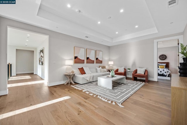 living room with light hardwood / wood-style flooring and a tray ceiling