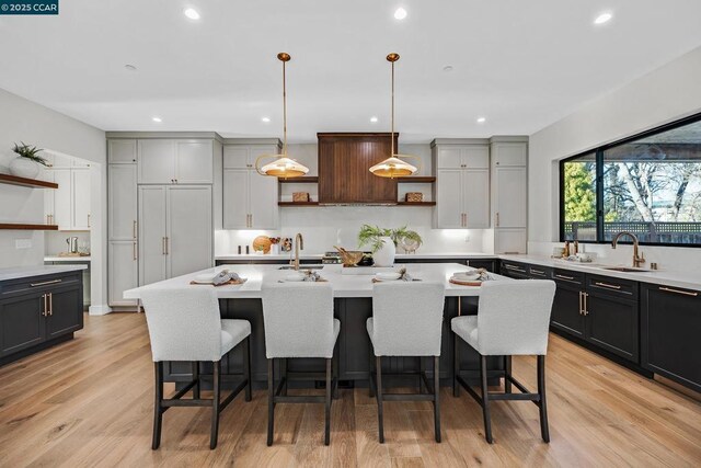 kitchen with an island with sink, gray cabinets, light hardwood / wood-style floors, and pendant lighting