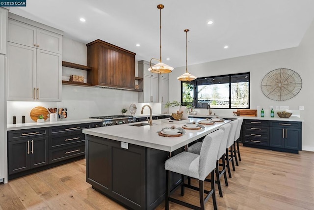 kitchen with hanging light fixtures, an island with sink, a kitchen bar, light wood-type flooring, and sink