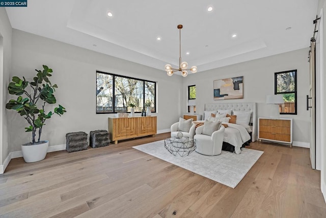 bedroom with light wood-type flooring, a tray ceiling, and a chandelier