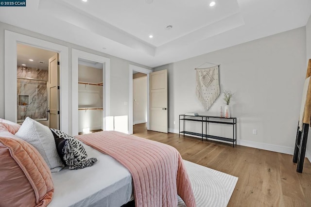 bedroom with ensuite bath, a spacious closet, a closet, light hardwood / wood-style floors, and a tray ceiling