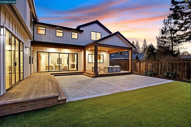 back house at dusk featuring a lawn, a wooden deck, and a patio area