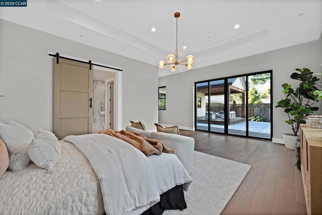 bedroom with a raised ceiling, a barn door, a chandelier, light wood-type flooring, and access to outside