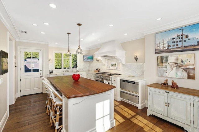 kitchen featuring custom range hood, butcher block countertops, a kitchen island, decorative light fixtures, and tasteful backsplash