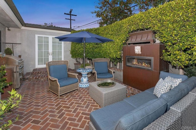 patio terrace at dusk with french doors, an outdoor living space with a fireplace, and grilling area