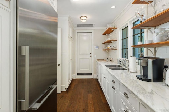 kitchen featuring sink, built in fridge, white cabinets, ornamental molding, and light stone countertops