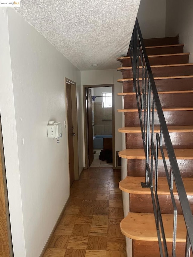 stairs with a textured ceiling and parquet floors